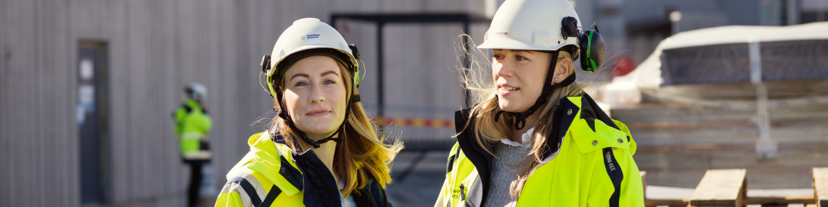 Två kvinnor med bygghjälmar och varseljackor på en byggarbetsplats