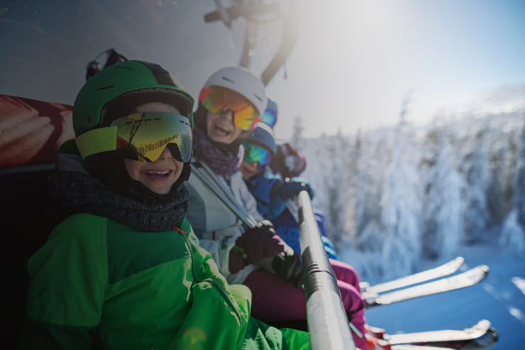 Family wearing ski equipment sitting in chair lift smiling at the camera.