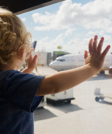 Toddler standing at a window looking at an airplane.