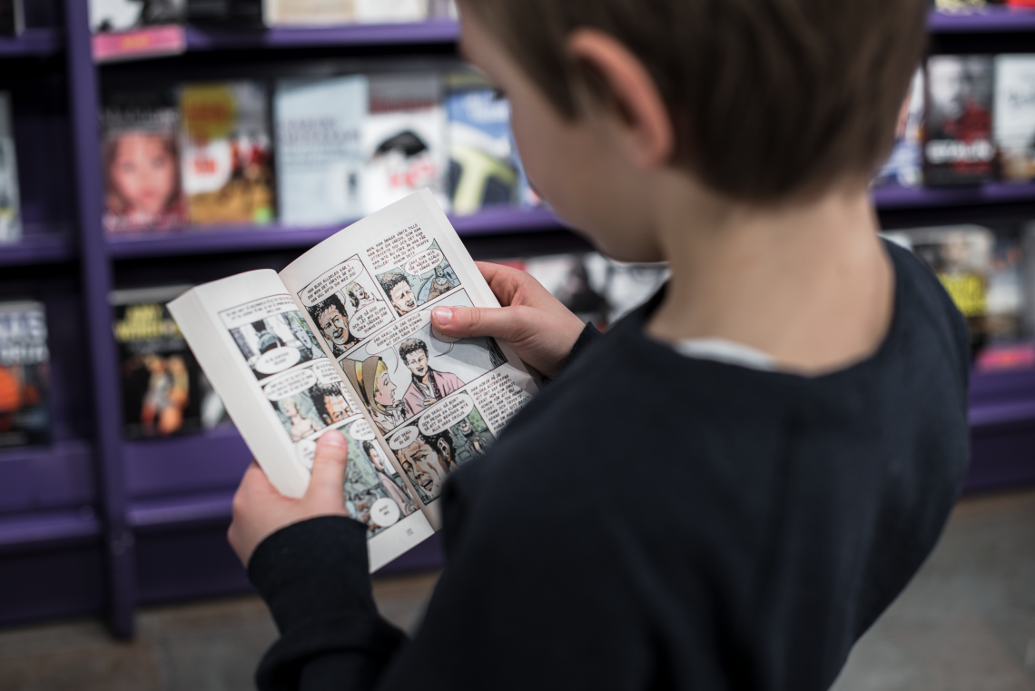 Boy standing up and reading a book at Pocket Shop at Stockholm Arlanda
