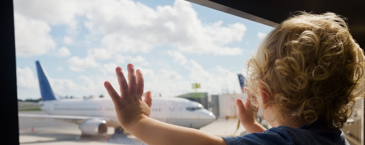 Litet barn står vid ett fönster och tittar på ett flygplan.