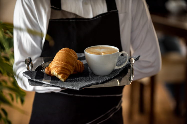 Servitör bär bricka med cappuccino and croissanter.