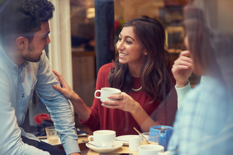 A group of three are drinking coffee and having a converesation.