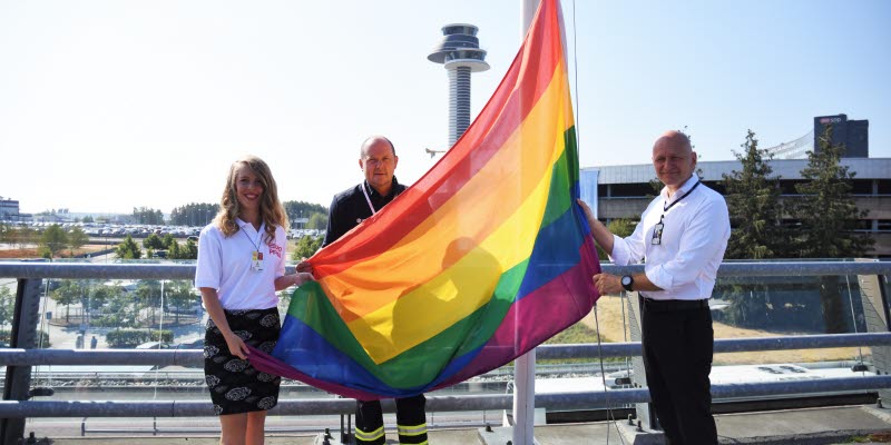 Prideflaggan hissas av tre personer på Arlanda