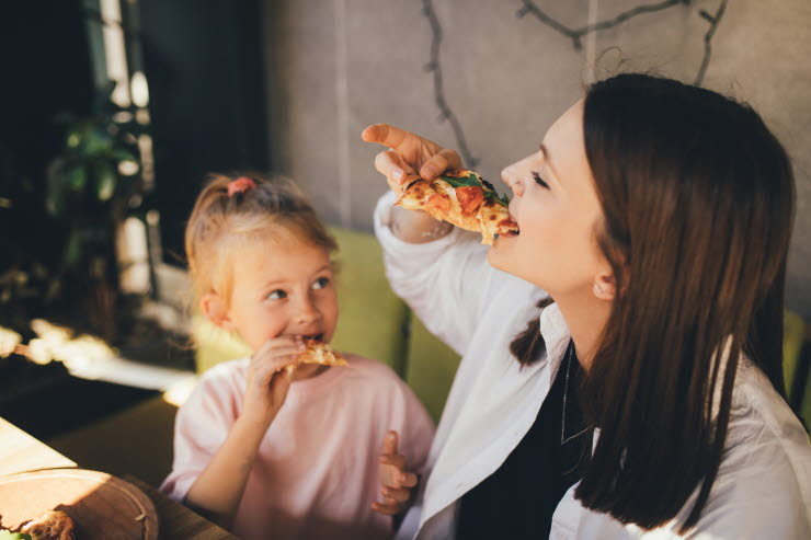 Ung kvinna och liten tjej äter pizza.