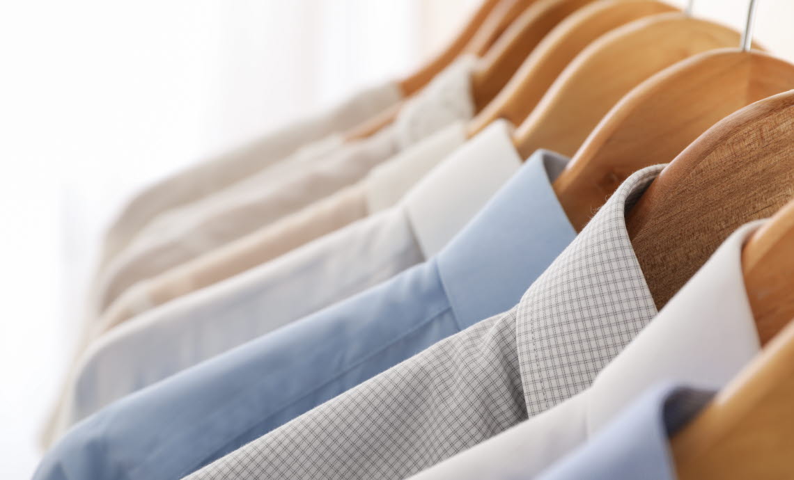 Close up of dress shirts in light colours on hangers.