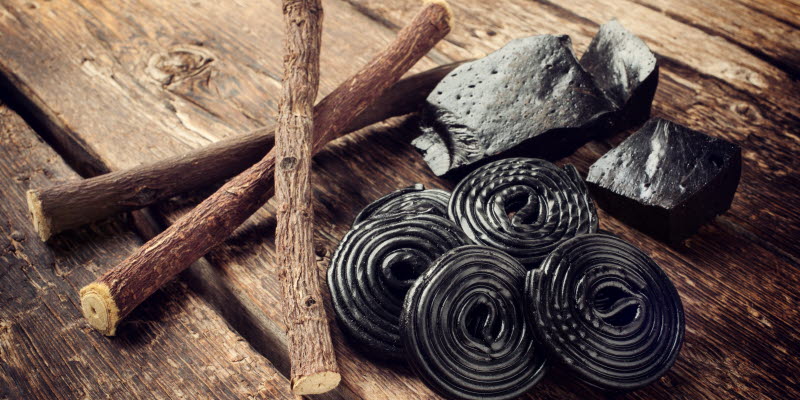 Licorice root, raw licorice and licorice candy swirls on wooden planks.