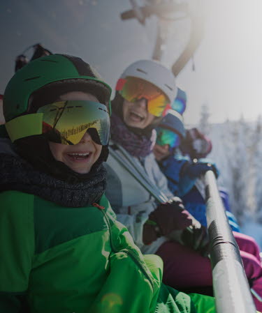 Family wearing ski equipment sitting in chair lift smiling at the camera.