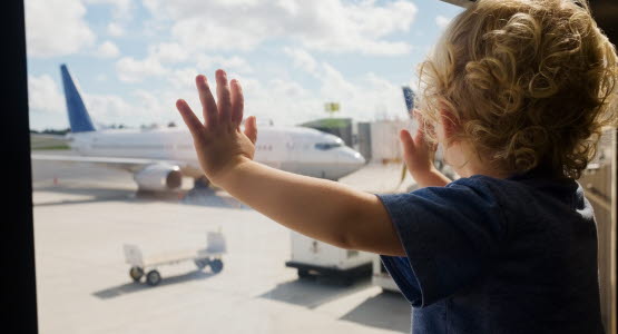 Toddler standing at a window looking at an airplane.