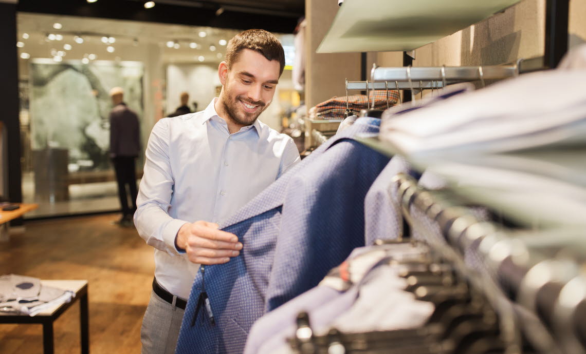 Man in clothing store looking at suit jacket.