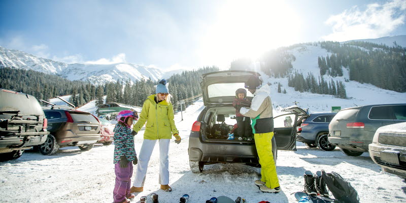 A mixed-race family in a parking lot unloading ski gear from their car during winter.