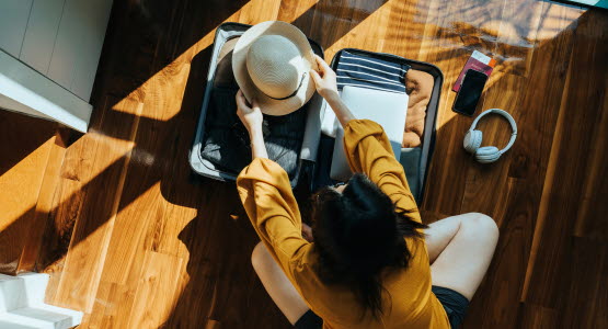 Overhead view of person sitting on the floor packing a small suitcase.