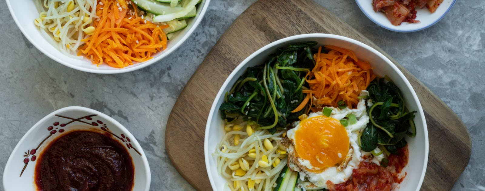Two bowls of bibimbap, and bowls with different sides.