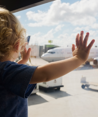 Litet barn står vid ett fönster och tittar på ett flygplan.