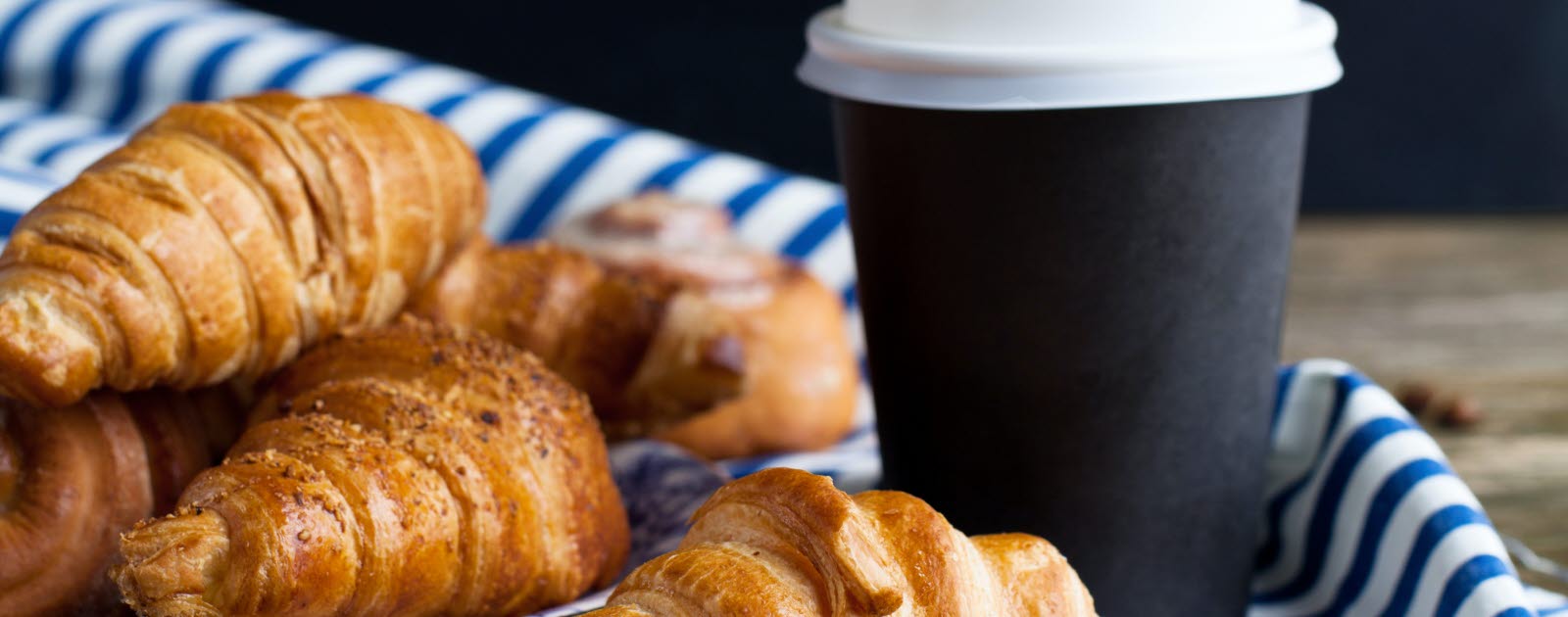 Plate of croissants and a to-go cup on wooden table.